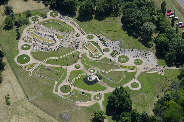 A képen egy park madártávlatból látható, különböző kör alakú és organikus formájú zöldterületekkel. A parkban sétautak, különböző növényekkel borított ágyások és kisebb emelvények találhatók. Az útvonalak között emberek sétálnak. Fák és füves területek szegélyezik a parkot, néhány parkoló autó is látható az egyik oldalon. Az egész terület geometrikus, esztétikus elrendezésű. (A kép forrása: Wikipedia)