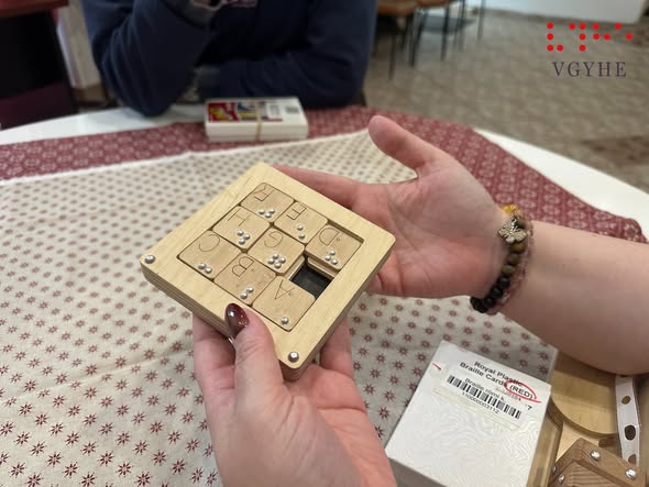 A képen egy résztvevő kezei látszanak, ahogy a Braille-Tili-Toli-játékot próbálja kirakni.