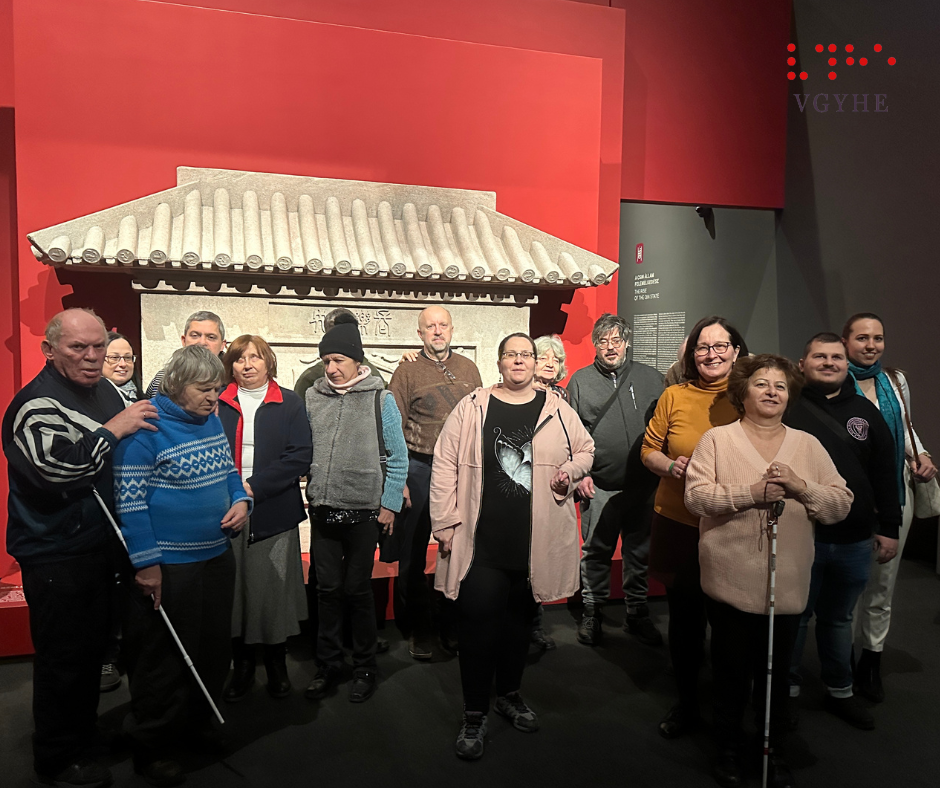 A képen a résztvevőkről készített csoportkép látható a Szépművészeti Múzeumban, háttérben a kiállítás elemeivel.