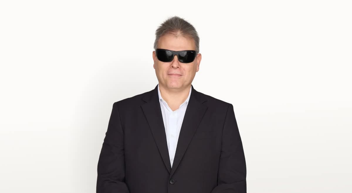 A képen dr. Kátai-Németh Vilmos látható, rövid, szürkésbarna hajjal. Fekete napszemüveget visel, ami eltakarja a szemeit. Fekete öltönyt és fehér inget hord. (A kép forrása: dr. Kátai-Németh Vilmos nyilvános Facebook-oldala)